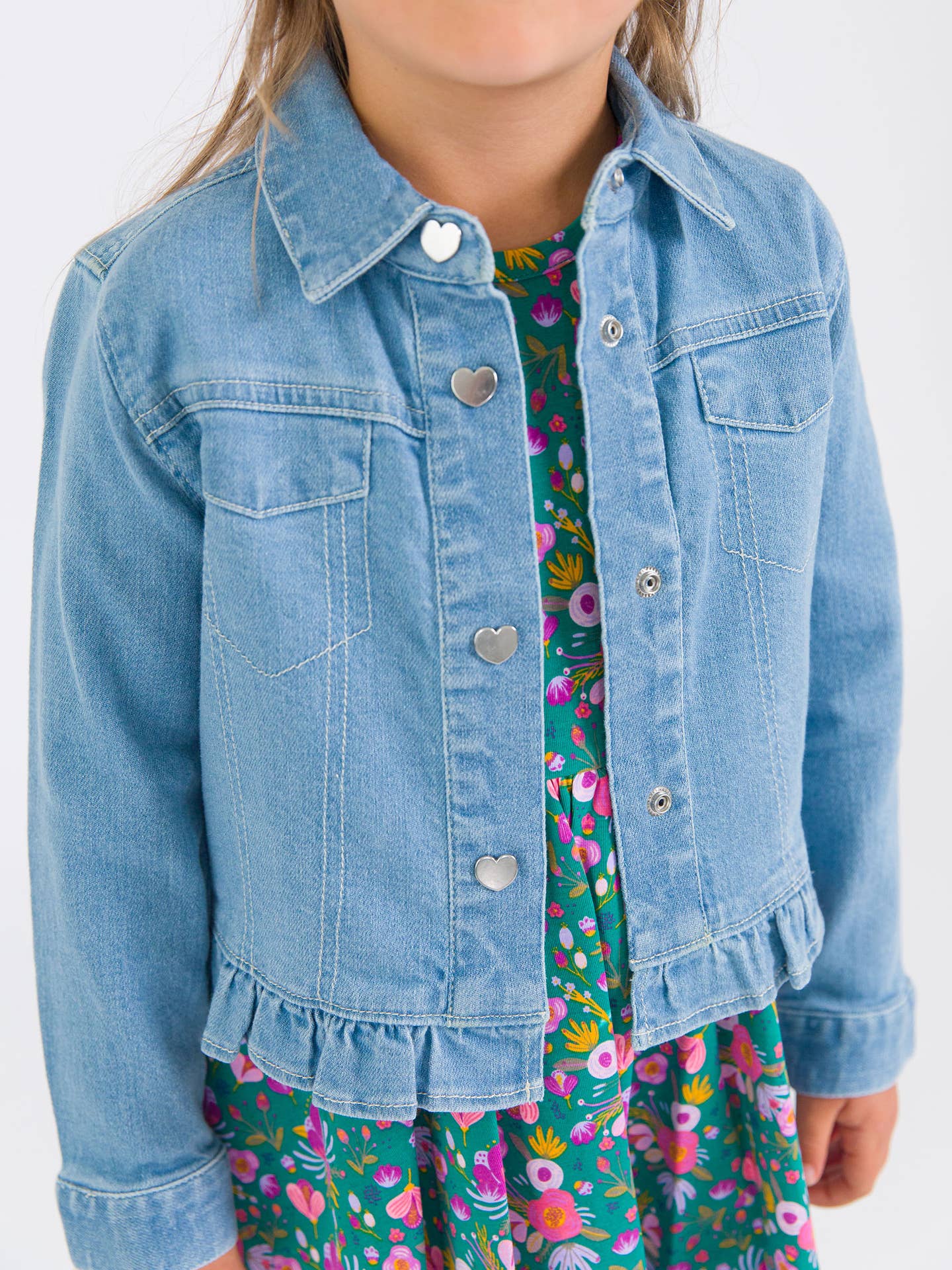 Model Wearing Rufflebutts & Ruggedbutts Girls Light Wash Denim Stretch Denim Ruffle Jean Jacket with Heart Buttons