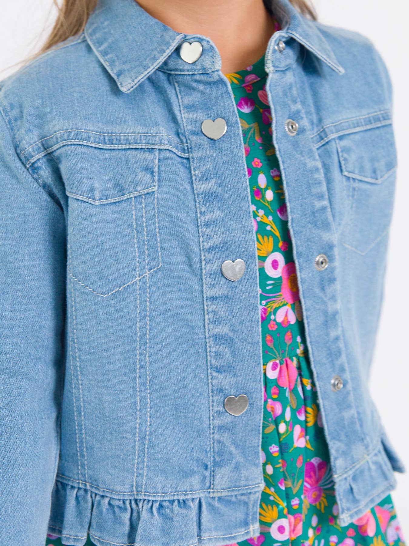 Model Wearing Rufflebutts & Ruggedbutts Girls Light Wash Denim Stretch Denim Ruffle Jean Jacket with Heart Buttons