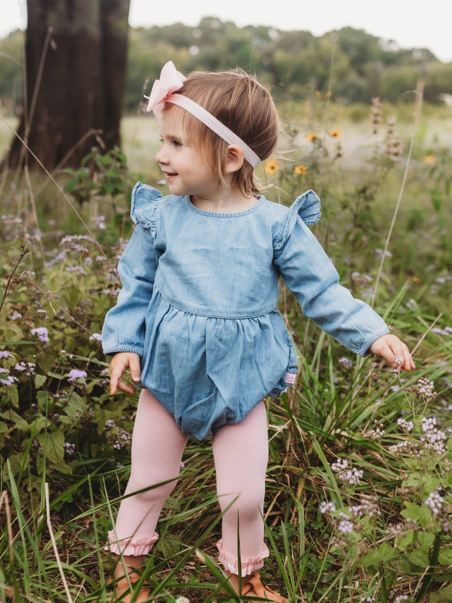 Model Wearing Rufflebutts + Ruggedbutts Baby Girls Light Wash Denim Long Sleeve Flutter Bubble Romper