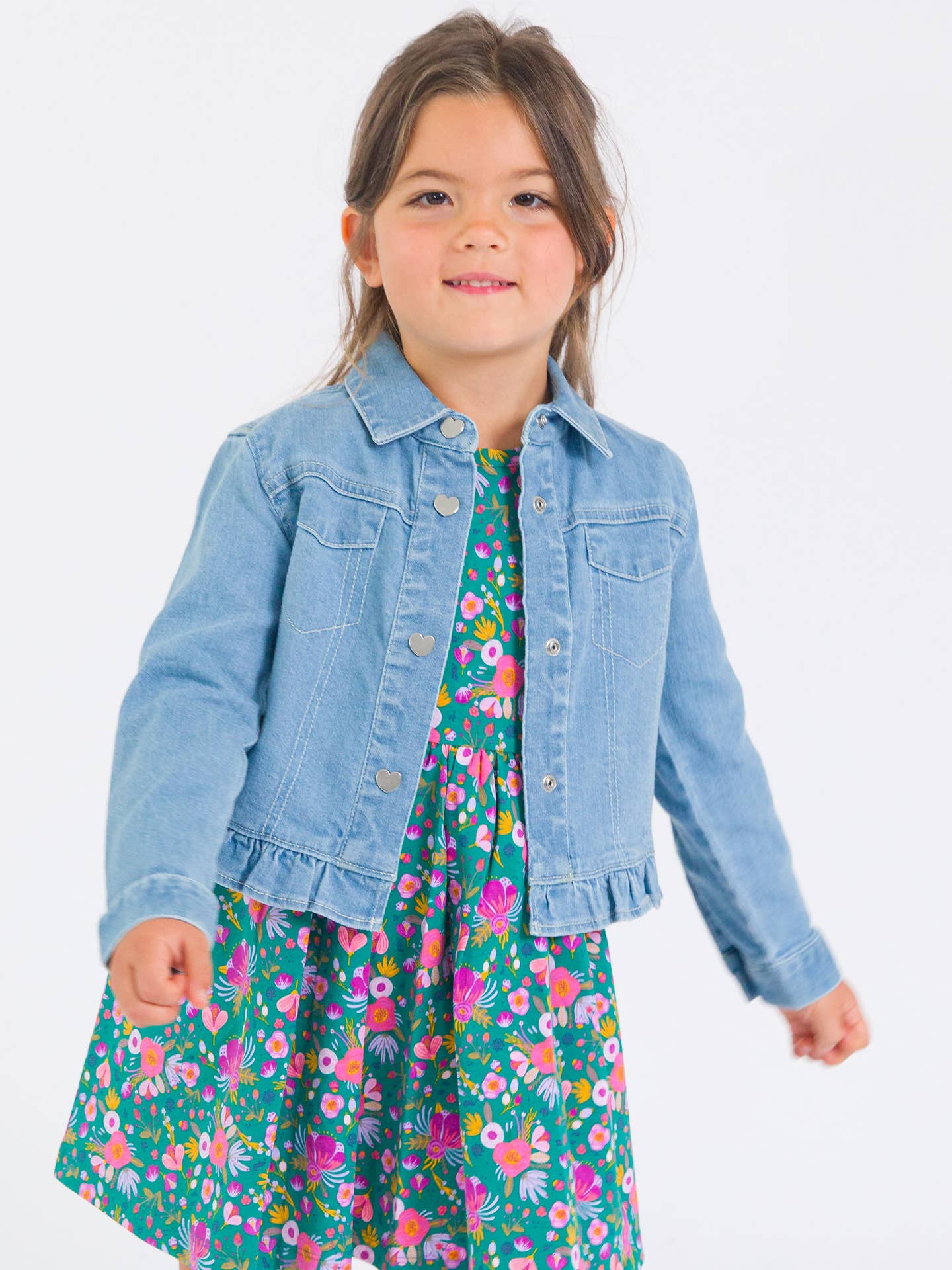 Model Wearing Rufflebutts & Ruggedbutts Girls Light Wash Denim Stretch Denim Ruffle Jean Jacket with Heart Buttons