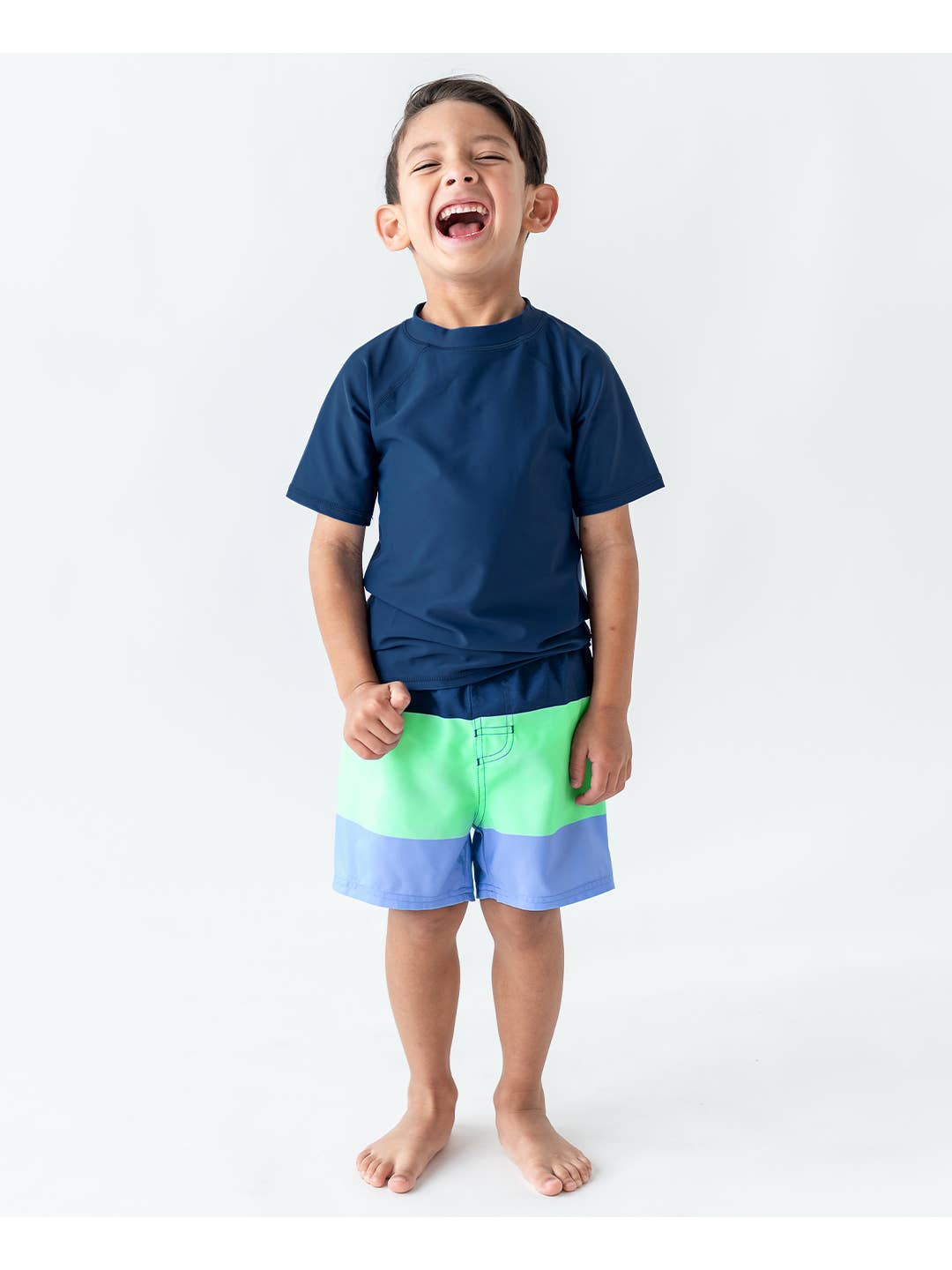 Model Wearing Rufflebutts + Ruggedbutts Boys Mint & Blue Color Block Swim Trunks and Navy short sleeve Rashguard 